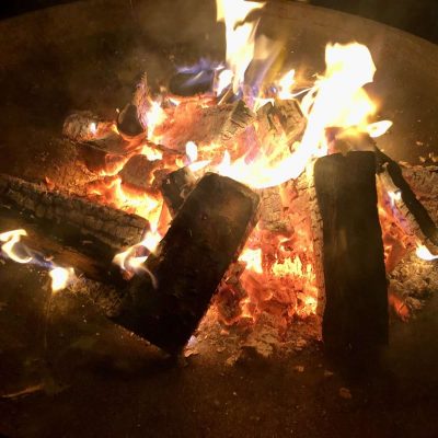 Holzscheite die brennen und Glut in einer Feuerschale am Lagerfeuer. Das Bild dient als Beispiel für ein schönes Erlebnis und ein tolles Paket bei einem Workshop in der Natur beim Gestaltcamp in Mannheim