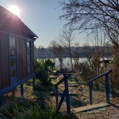 Pavillon Stollenwörthweiher Gestaltcamp Mannheim Man sieht die Location für den Outdoor-Workshop in Mannheim vom Gestaltcamp. Die Sonne scheint auf den Stollenwörthweiher in Mannheim, man sieht ein Lagerfeuer und den Pavillon aus Holz als Unterschlupf bei Regen