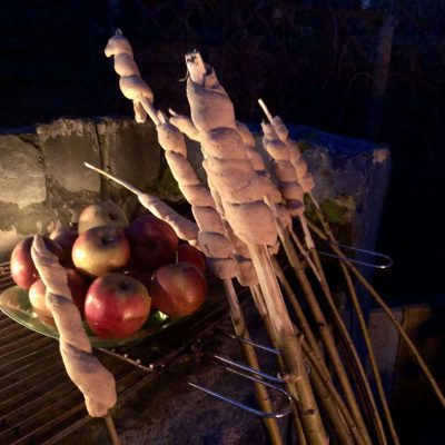 An einen Grill gelehnt sieht man liebevoll gemachtes, gesundes Stockbrot sowie Bratäpfel für einen tollen Workshop im Gestaltcamp inklusive outdoor cooking für eine echte Auszeit in der Natur. Outdoor-Workshop Kleine Visionssuche am Lagerfeuer am 28. Mai 22 in Mannheim mit Julie Strobach und Jennifer Schumacher-Hetzel am Stollenwörthweiher vom Gestaltcamp - Gestalttherapie in Mannheim und Waldpädagogik